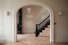 an arched doorway leading to a hallway with wooden floors and white walls, along with a black door