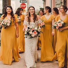 a group of women standing next to each other wearing yellow dresses and holding bouquets