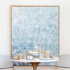 two chairs and a table in front of a blue wall with white marbled paint