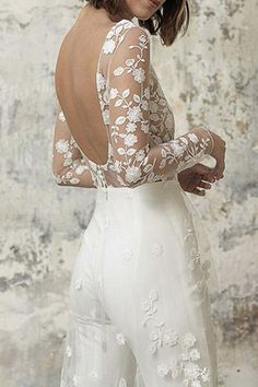 the back of a woman's wedding dress, with white flowers on it and long sleeves