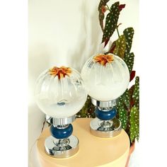 two glass vases with flowers on them sitting on a table next to a cactus