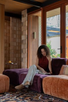 a woman sitting on top of a purple couch in front of a large glass window