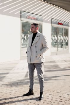 a man standing in front of a building with his hands in his pockets and looking off to the side