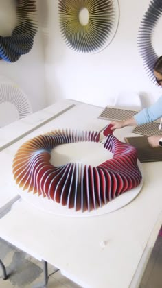 a woman is working on a sculpture in a room with white walls and circular mirrors