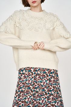 a woman wearing a white sweater and floral print skirt with her hands on her hips