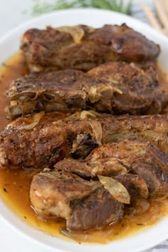 some meat is sitting on a plate covered in sauce and garnished with herbs