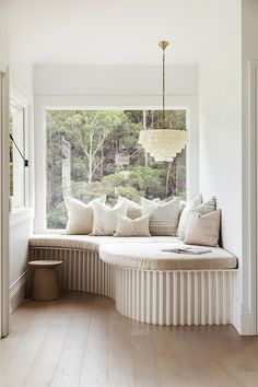 a large window seat with pillows on it in front of a white wall and wooden floor