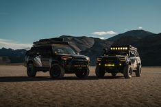 two vehicles parked in the desert with mountains in the background