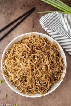 a white bowl filled with noodles next to chopsticks and a napkin on the side