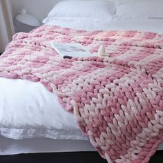 a pink and white blanket sitting on top of a bed next to a pillow in a bedroom