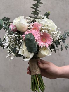 a person holding a bouquet of white and pink flowers with greenery on the stems