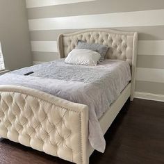 a white bed sitting next to a window in a room with striped walls and wooden floors