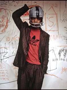 a young man wearing a helmet standing in front of a wall with graffiti on it