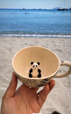 a hand holding a cup with a panda bear painted on it