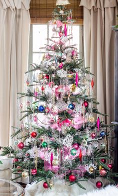 a decorated christmas tree in front of a window with pink and green ornaments on it