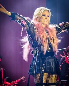 a woman with pink hair and black outfit on stage holding her arms out in the air