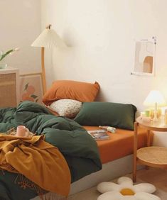 an unmade bed with green and orange sheets in a white room next to a wicker side table