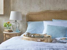 a tray with food on top of a bed next to a night stand and lamp