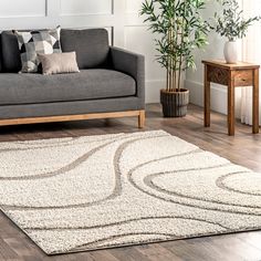 a living room with a gray couch and white rugs on the wooden floor next to a potted plant