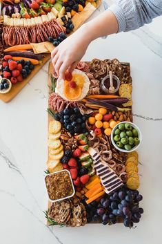 a platter filled with fruit, crackers and cheeses is being held by a person