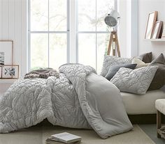 a bedroom with white walls and flooring has a large bed covered in grey comforter