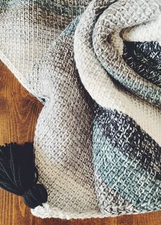 a pile of blankets sitting on top of a wooden floor next to a ball of yarn