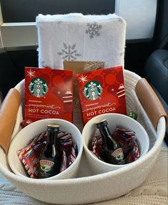 two starbucks mugs are sitting in a basket with hot cocoa packets and candy bars