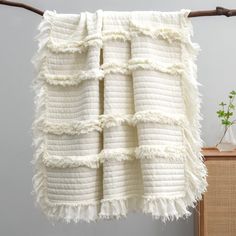 a white blanket hanging on a clothes line next to a wooden cabinet with a plant in it