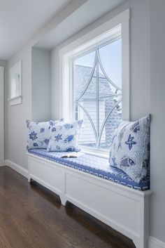 a window seat with pillows on it in front of a wooden floor and white walls