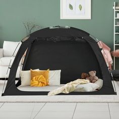 a black tent with pillows and blankets on the floor in a living room next to a white couch