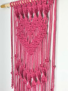 a pink crocheted wall hanging on a white wall with a wooden stick in front of it