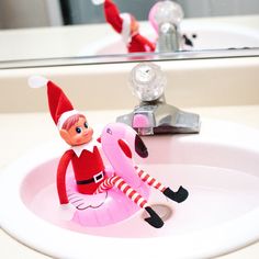 an elf is sitting in the sink with a pink flamingo toy next to it