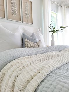 a bed with white sheets and pillows in a bedroom next to two framed pictures on the wall