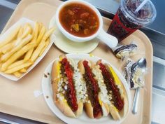 hot dogs and french fries are on a tray next to a bowl of soup, water and soda