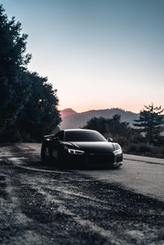 a black sports car parked on the side of a road at sunset or dawn with trees and mountains in the background