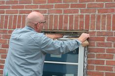 a man is working on the side of a brick building with a window pane