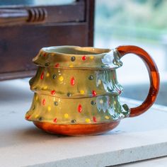 a ceramic coffee cup sitting on top of a counter next to a window sill