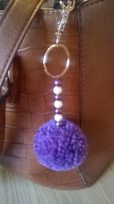 a purple pom - pom keychain hanging from a brown purse