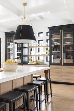 a kitchen with black cabinets and white countertops, an island in the center is flanked by four stools