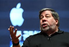 a man in black shirt talking on stage with an apple logo behind him and his hands out