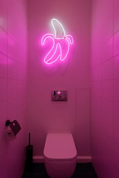 a pink bathroom with a toilet and neon lights on the wall above it's tank