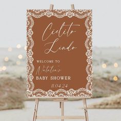 a welcome sign for a baby shower is displayed on an easel with lights in the background