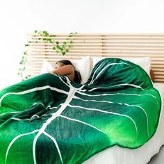 a woman laying on top of a bed covered in a green leafy comforter