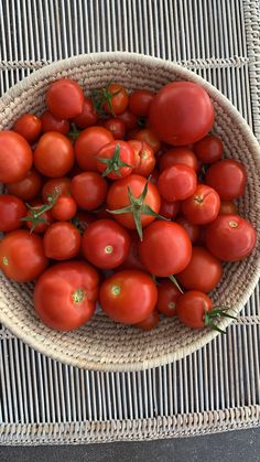 a wicker basket filled with lots of ripe red tomatoes on top of a table