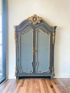 an antique blue armoire with gold trimmings on the top and bottom, against a white wall