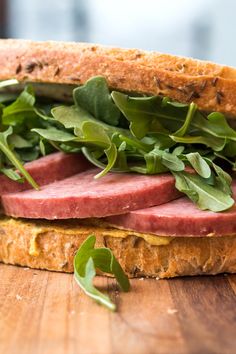 a close up of a sandwich with meat and greens on a wooden surface, ready to be eaten