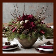 a vase filled with pine cones and red flowers on top of a table next to plates