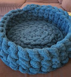 a blue crocheted dog bed sitting on top of a brown couch next to a pillow