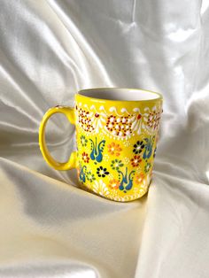 a yellow coffee cup sitting on top of a white cloth covered tablecloth with an artistic design