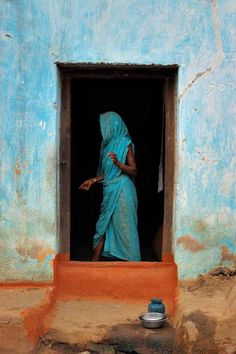 a woman in a blue sari is standing at the entrance to her home, looking out